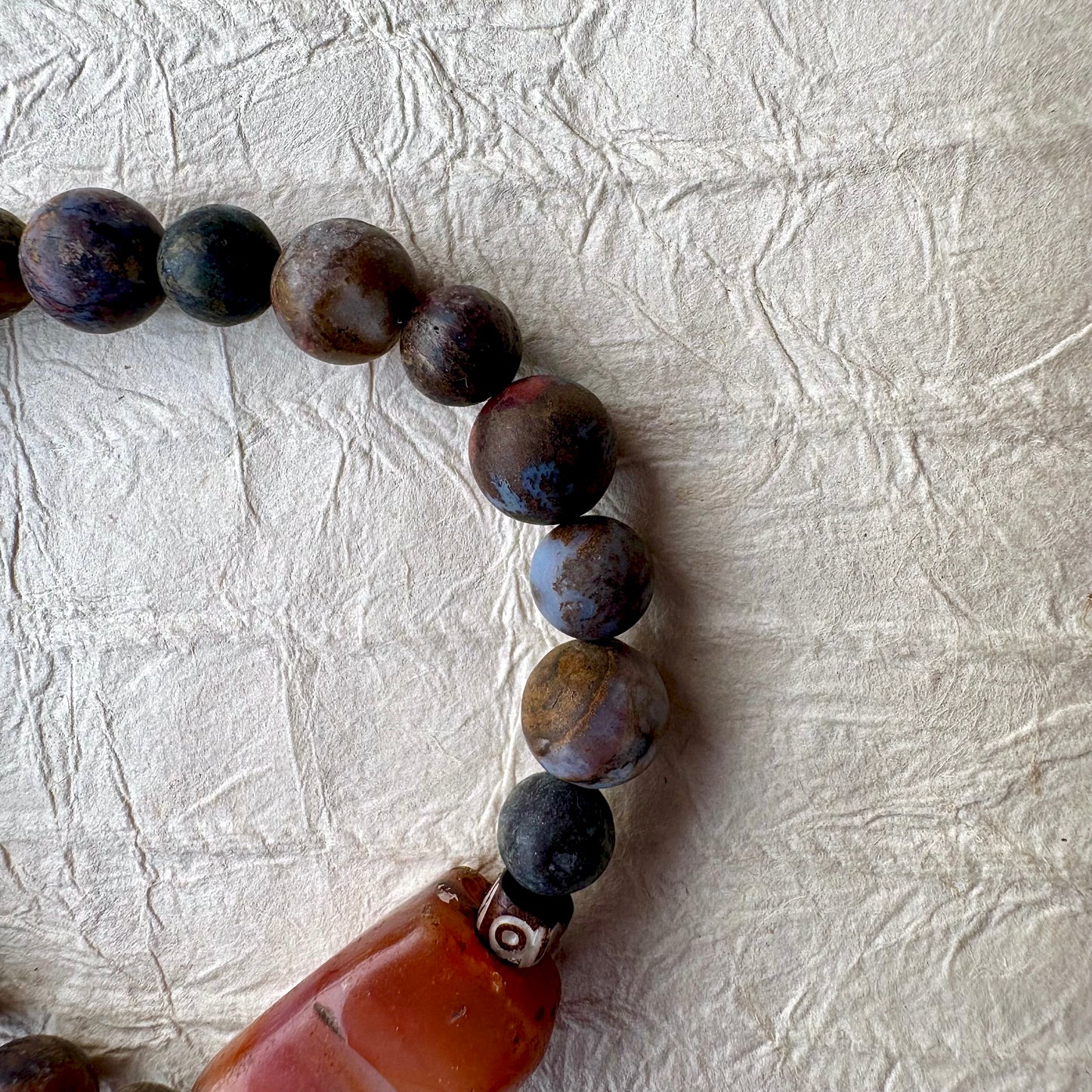 A beaded bracelet made of dark brown and black marbled beads with a large rectangular carnelian gemstone.
