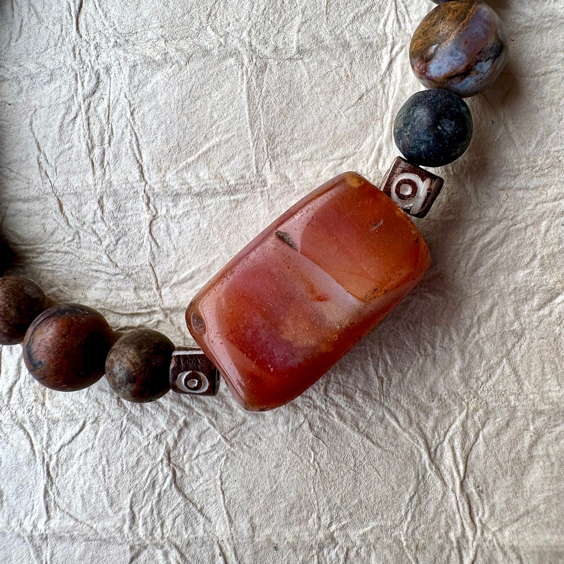 A beaded bracelet made of dark brown and black marbled beads with a large rectangular carnelian gemstone.