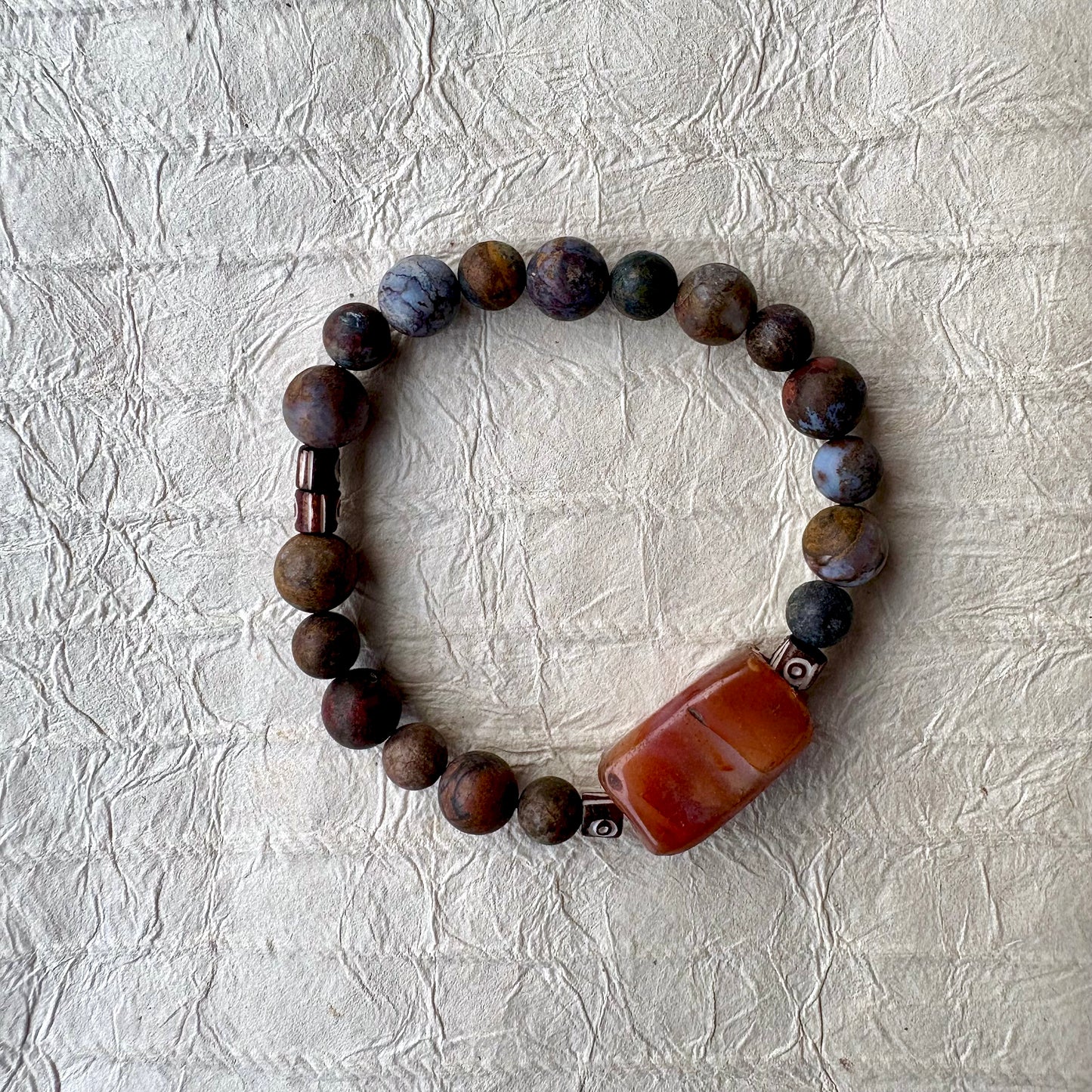 A beaded bracelet made of dark brown and black marbled beads with a large rectangular carnelian gemstone.