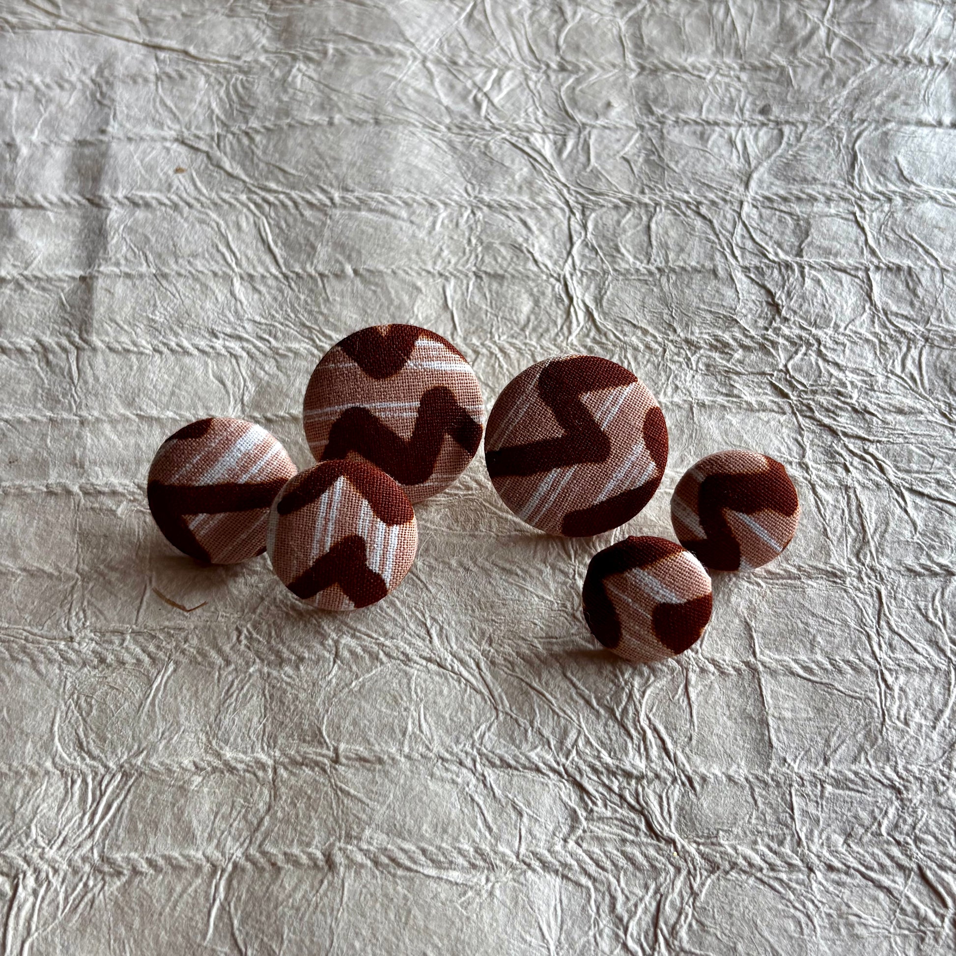 Five round fabric-covered earrings with a brown and beige zigzag pattern.