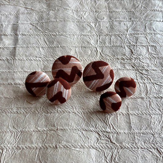 Five round fabric-covered earrings with a brown and beige zigzag pattern.