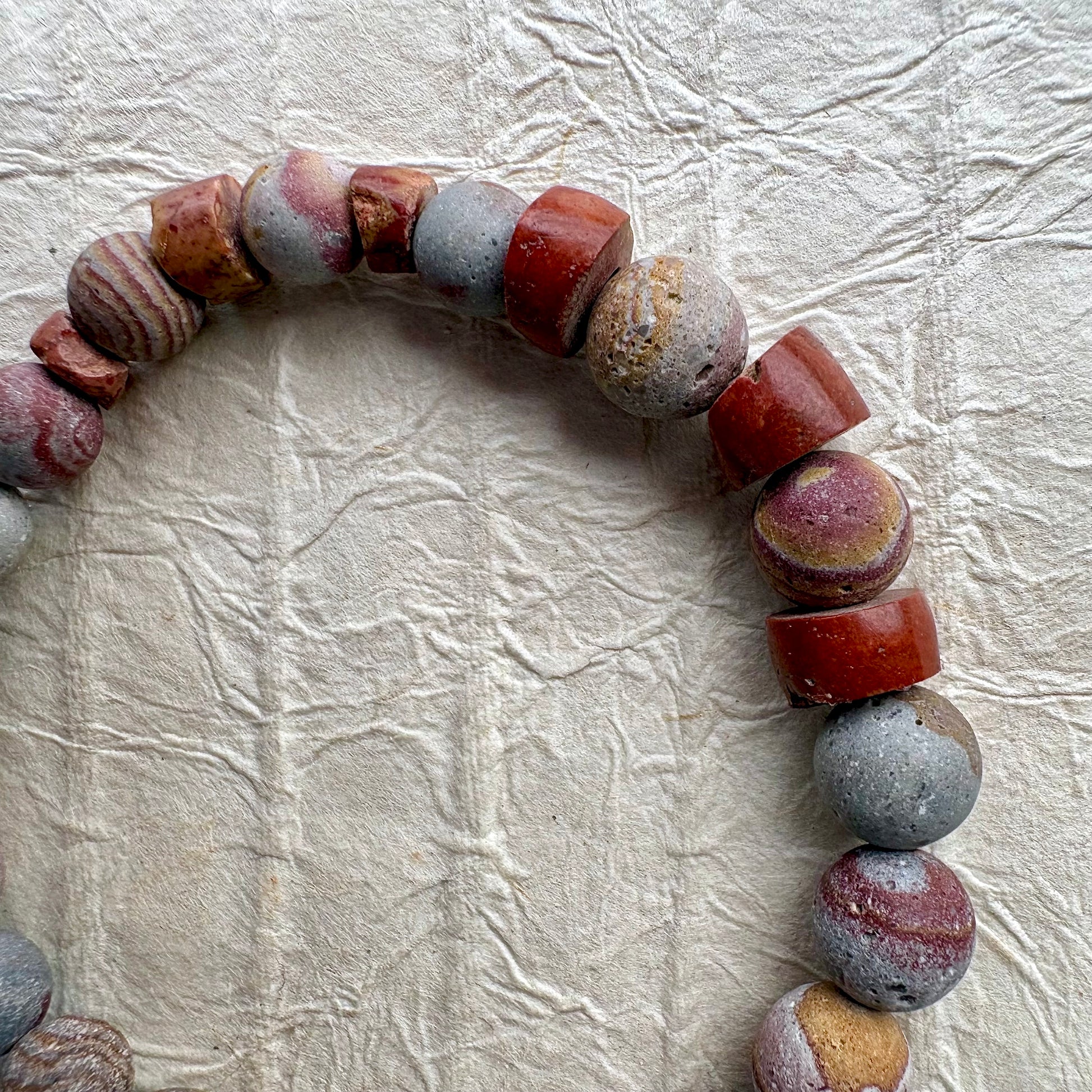A beaded stretch bracelet made of polished stone beads in earthy red, gray, and brown tones.