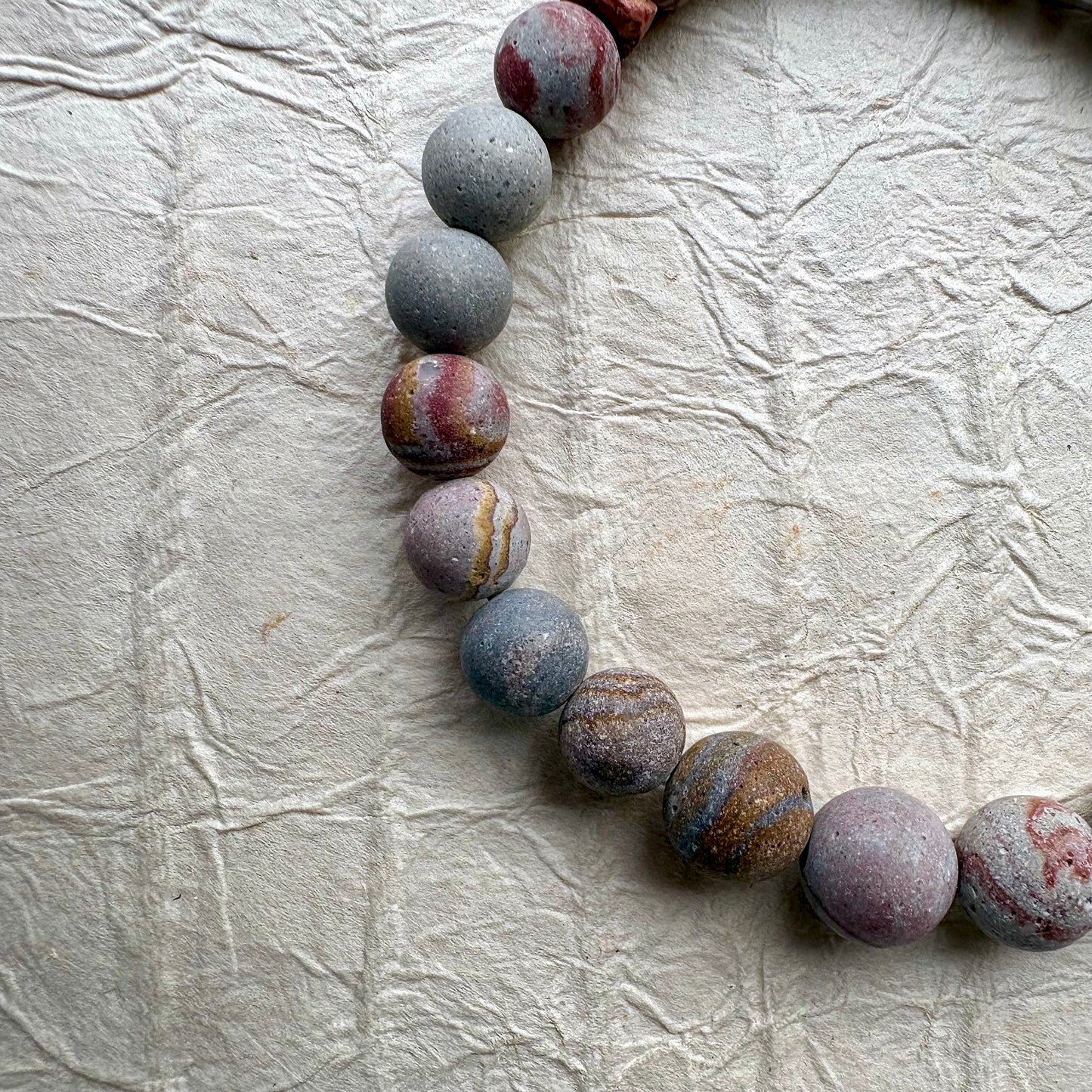 A beaded stretch bracelet made of polished stone beads in earthy red, gray, and brown tones.