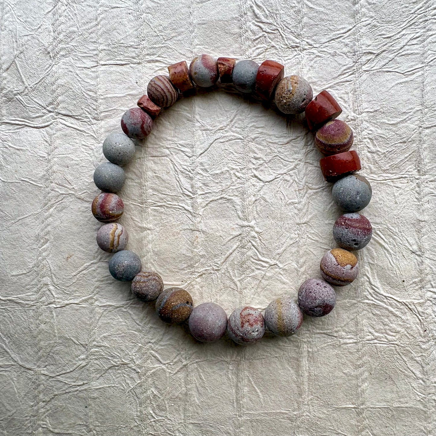 A beaded stretch bracelet made of polished stone beads in earthy red, gray, and brown tones.