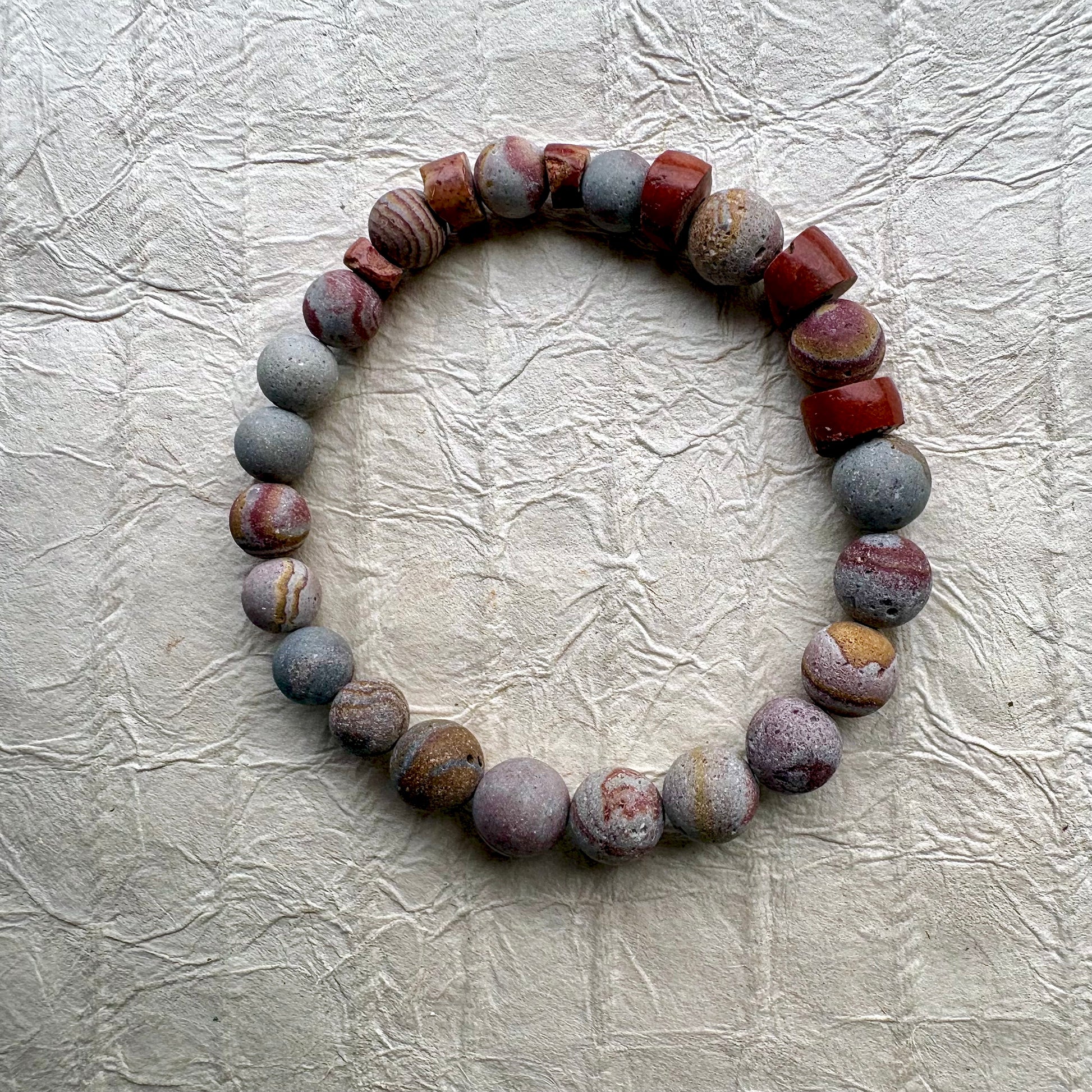A beaded stretch bracelet made of polished stone beads in earthy red, gray, and brown tones.