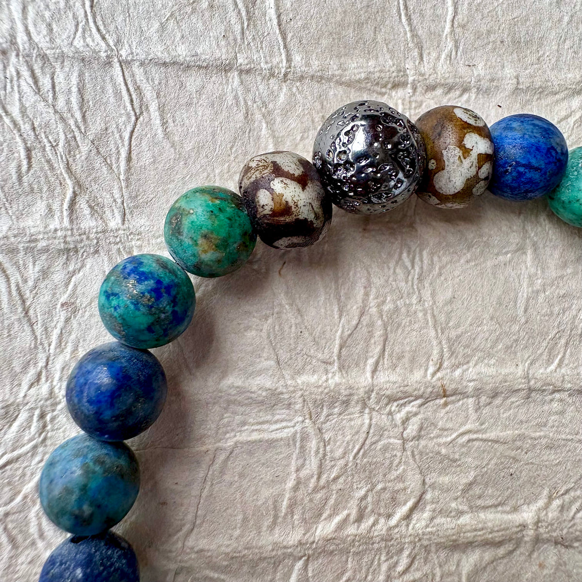 A beaded stretch bracelet made of polished round gemstone beads in blue, green, gunmetal, and brown.