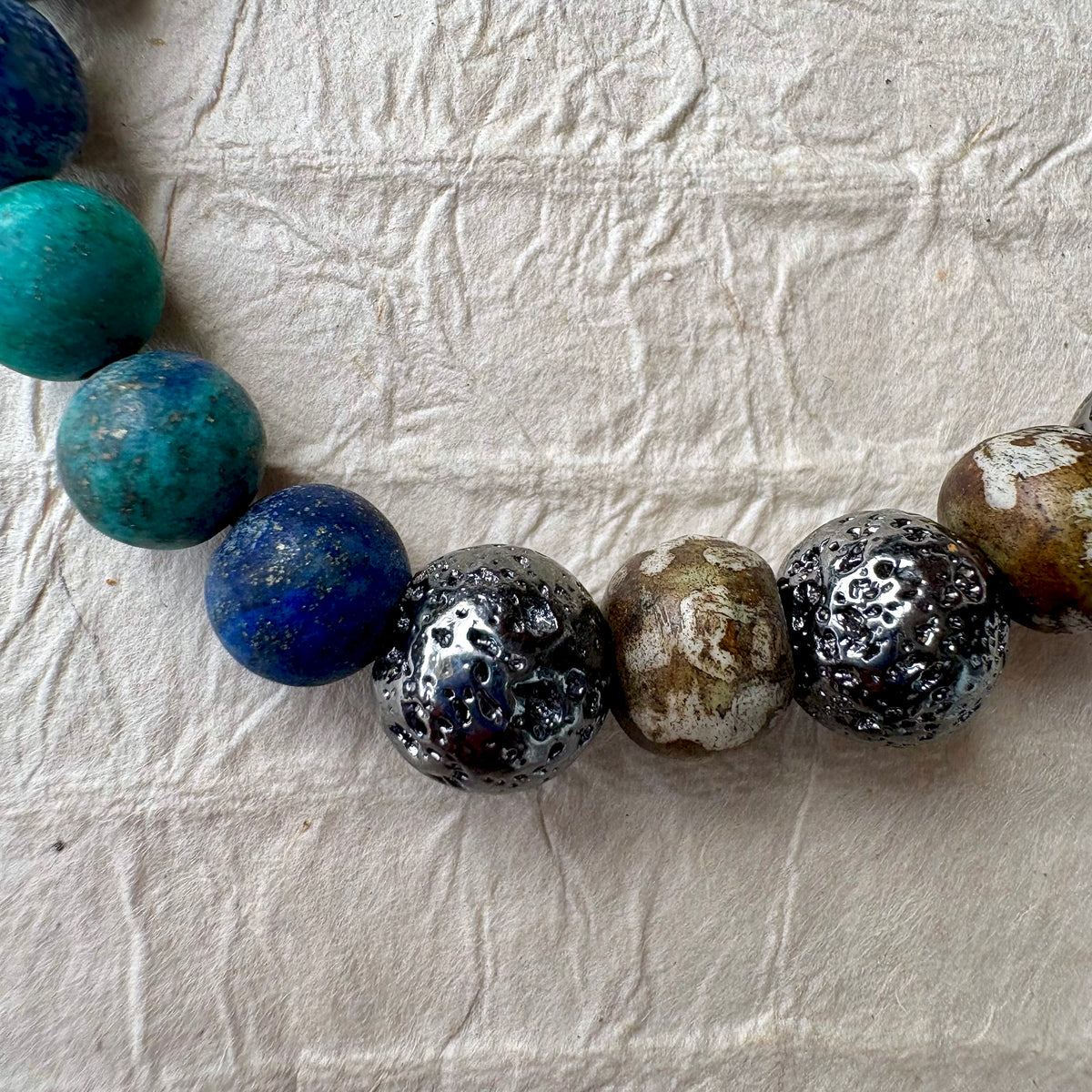 A beaded stretch bracelet made of polished round gemstone beads in blue, green, gunmetal, and brown.