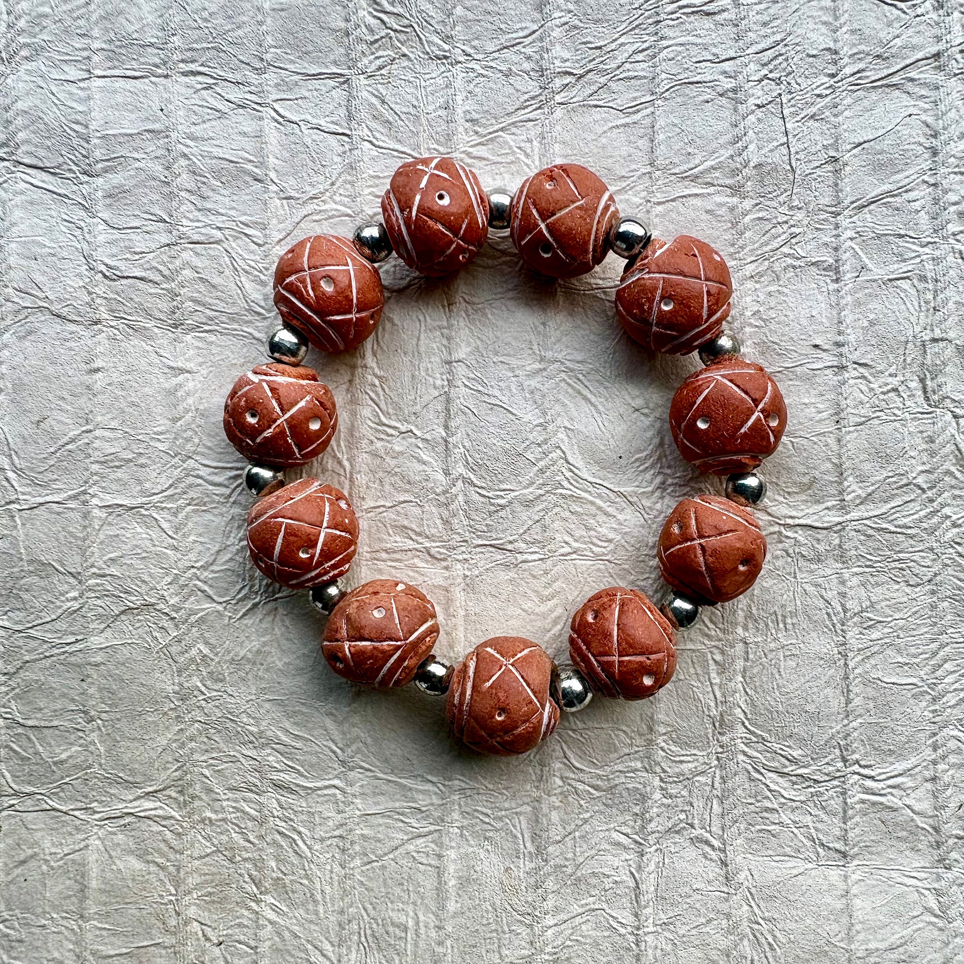 A beaded stretch bracelet made of reddish-brown carved wooden beads with white painted geometric patterns, separated by small metallic silver beads.