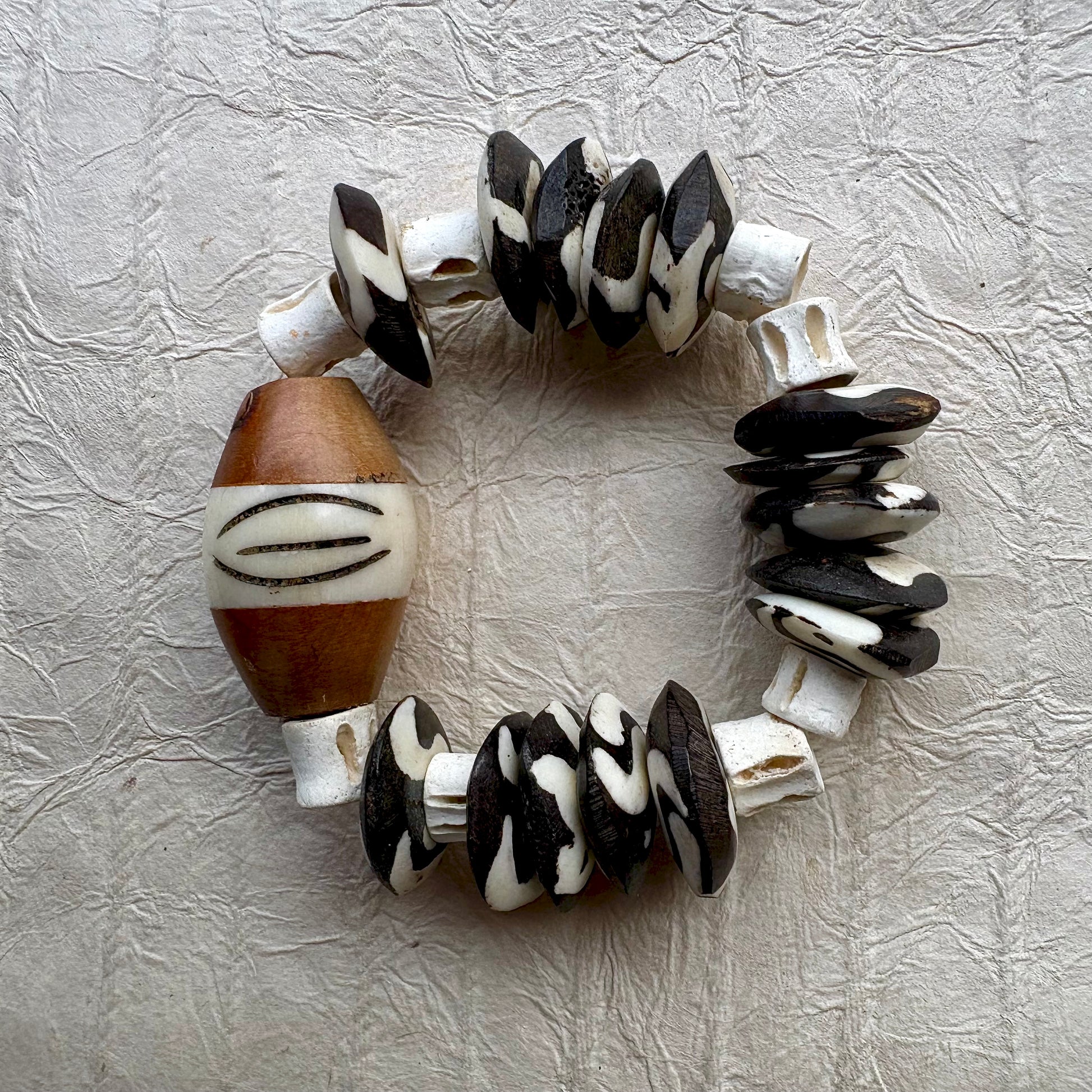 A handmade beaded bracelet made of alternating black and white patterned beads and a large brown and white accent bead, displayed on a textured light gray background.