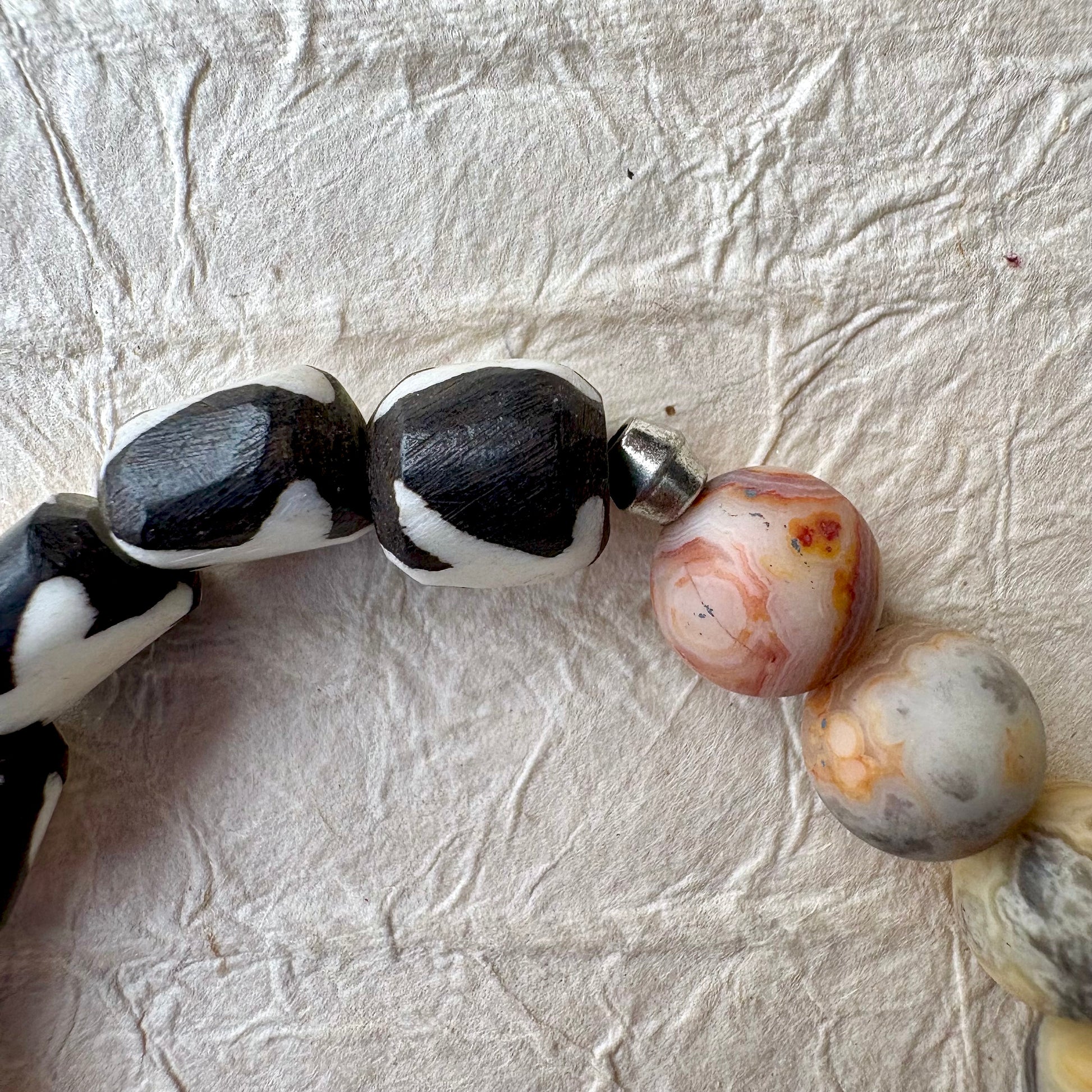 A close-up of a beaded strand with irregular black-and-white marbled beads and smooth round agate-like beads in pink, gray, and cream tones.